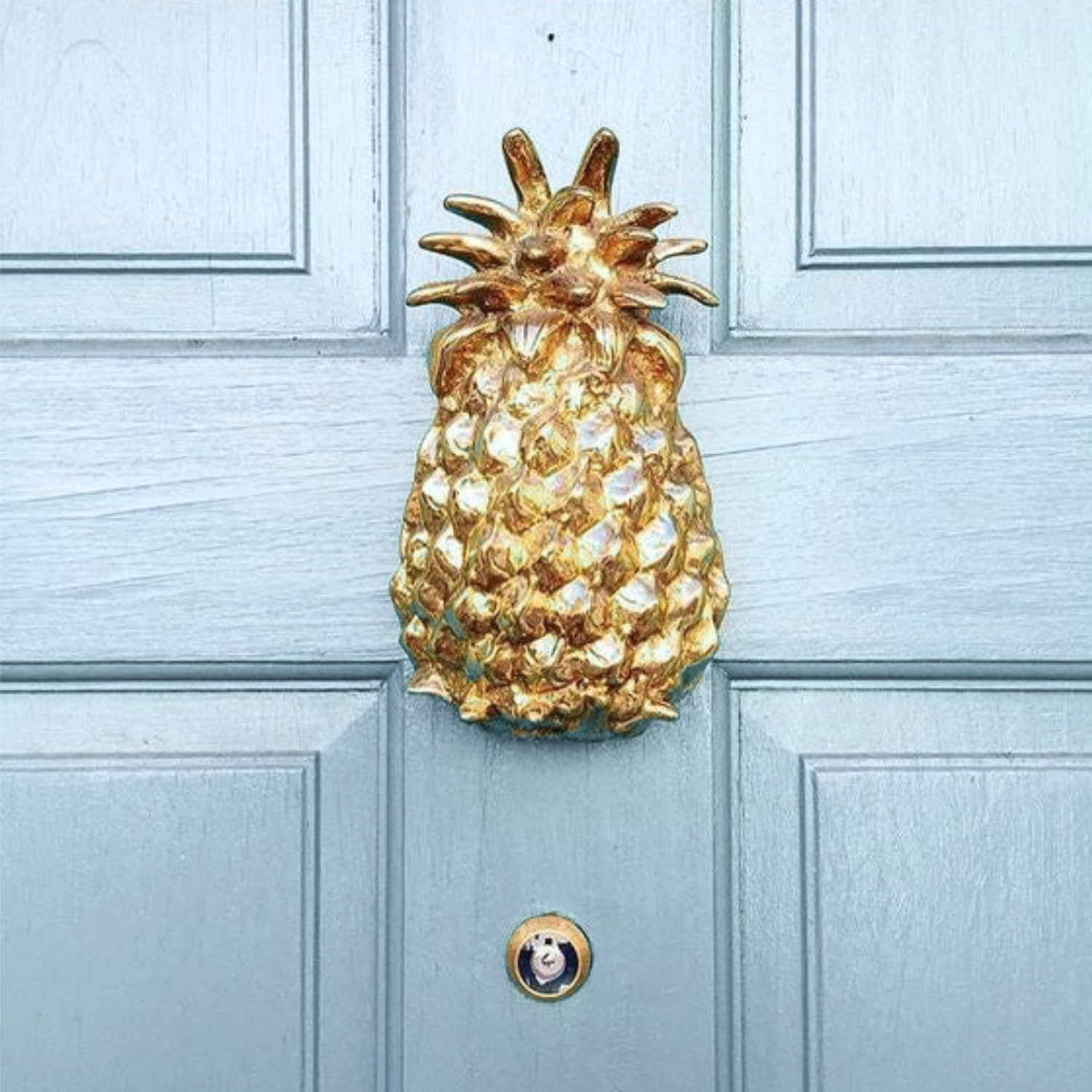 Gold pineapple door knocker on a light blue door